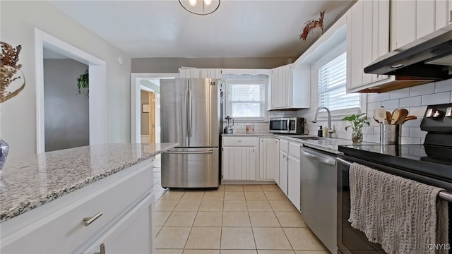 kitchen featuring light tile patterned floors, stainless steel appliances, decorative backsplash, a sink, and wall chimney exhaust hood