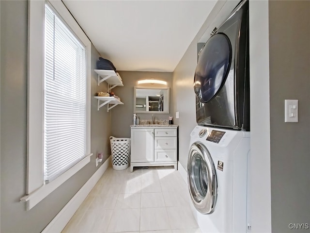 clothes washing area with light tile patterned flooring, a sink, stacked washer and clothes dryer, and baseboards