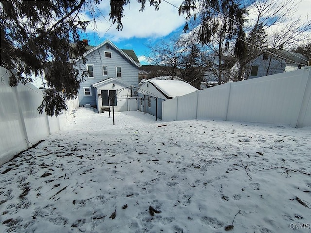 snow covered house featuring a fenced backyard