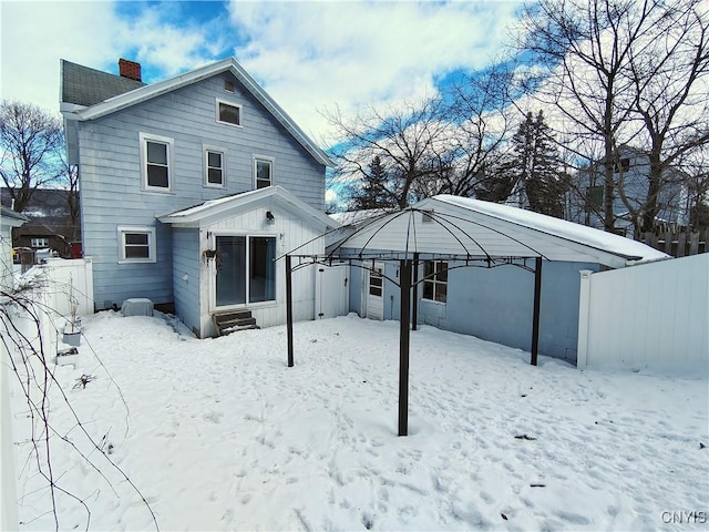 snow covered house featuring fence, a chimney, and a gazebo