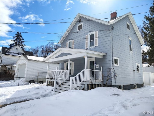 view of front of home featuring covered porch, a chimney, a detached garage, and fence