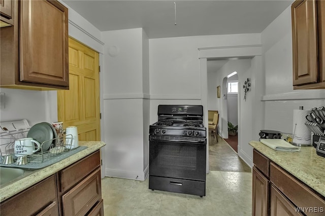 kitchen featuring light stone countertops, baseboards, arched walkways, and gas stove