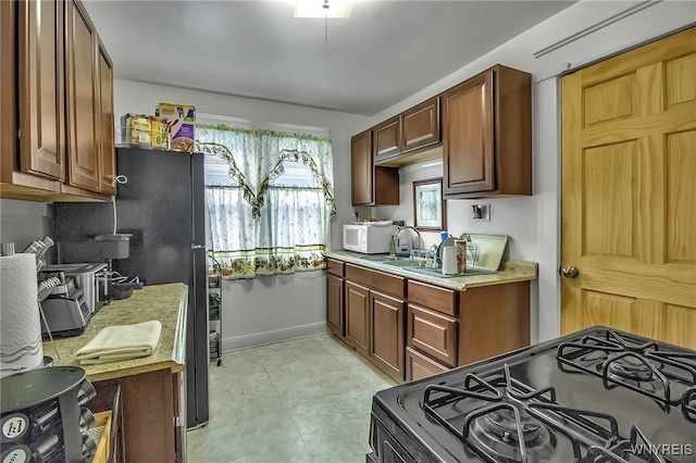 kitchen with white microwave, a sink, baseboards, light countertops, and gas range oven