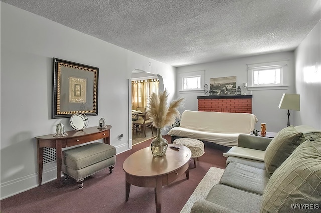 carpeted living area featuring arched walkways, a healthy amount of sunlight, a textured ceiling, and baseboards