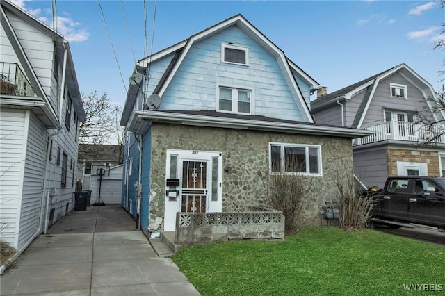 dutch colonial with stone siding, a front lawn, an outdoor structure, and a gambrel roof