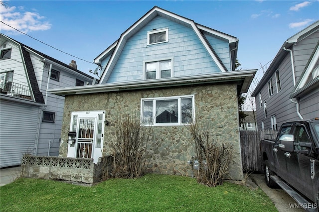 back of property featuring stone siding, a lawn, a gambrel roof, and fence