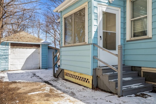 snow covered property featuring entry steps, a detached garage, and an outbuilding