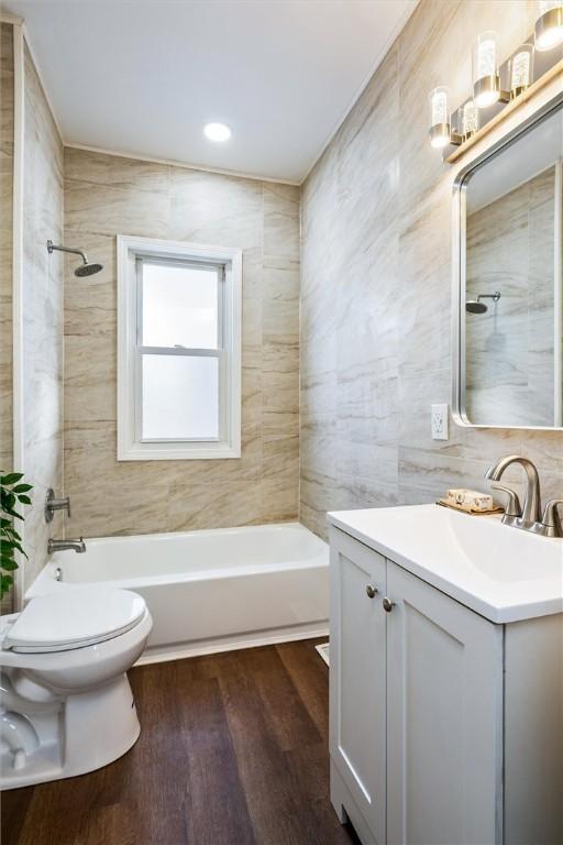 bathroom featuring shower / washtub combination, tile walls, toilet, vanity, and wood finished floors