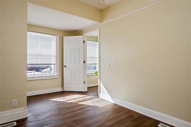 empty room with dark wood-style floors, visible vents, and baseboards