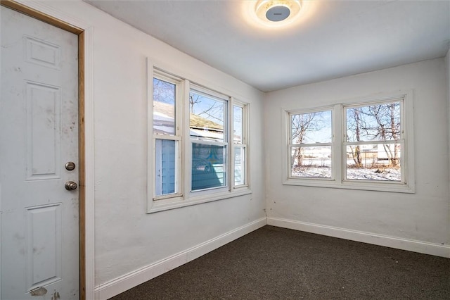 spare room with dark colored carpet and baseboards