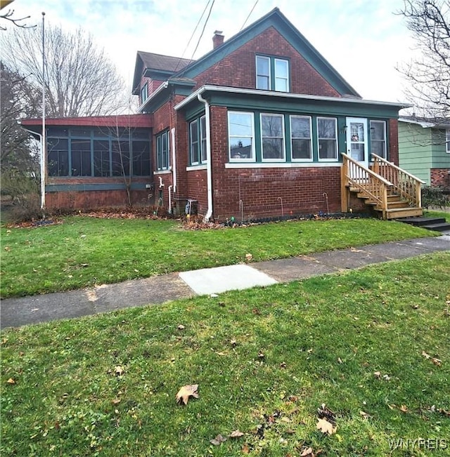 view of front of house with a front yard, a sunroom, a chimney, entry steps, and brick siding