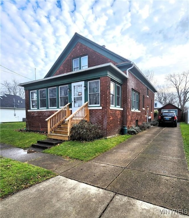 bungalow-style home featuring brick siding, a front lawn, concrete driveway, and an outdoor structure