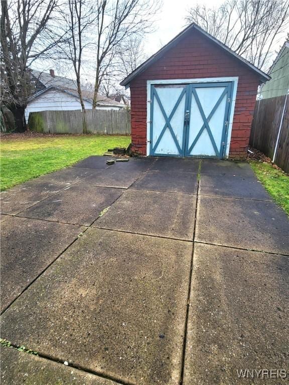 view of outbuilding featuring concrete driveway, fence, and an outbuilding