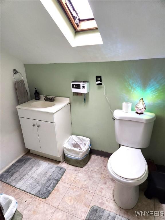 half bath with vanity, baseboards, vaulted ceiling with skylight, tile patterned flooring, and toilet