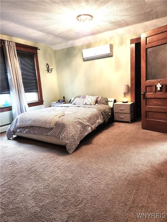 bedroom with light carpet, a textured ceiling, and a wall mounted air conditioner