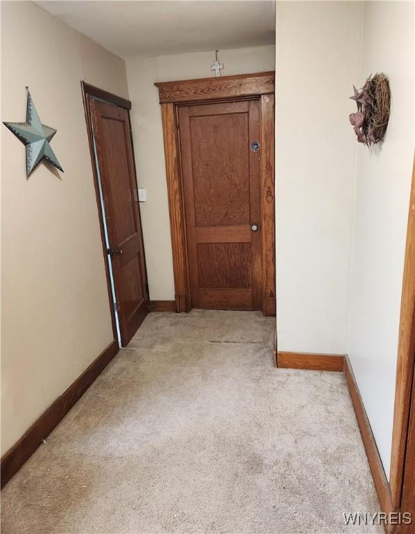 hall featuring baseboards and light carpet