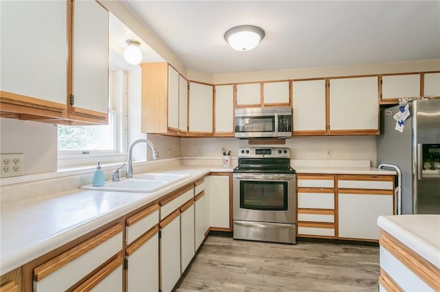 kitchen with light wood-style flooring, stainless steel appliances, a sink, and light countertops