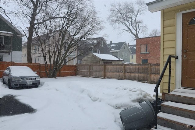 yard covered in snow featuring entry steps, fence, and a residential view