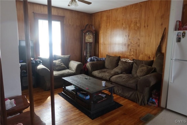 living room with light wood-style floors, wood walls, and ceiling fan