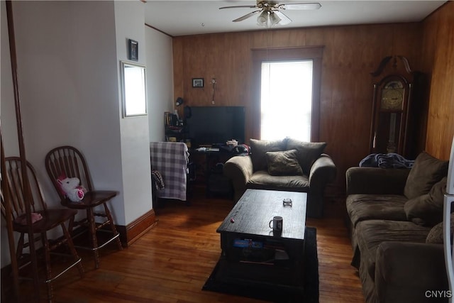 living area featuring baseboards, a ceiling fan, wood walls, and dark wood-type flooring
