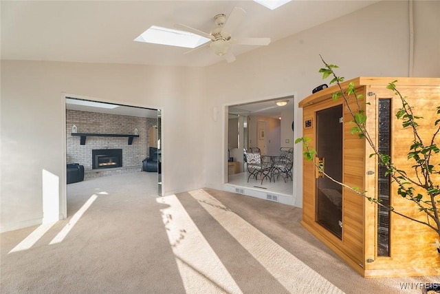 interior space with lofted ceiling with skylight, a brick fireplace, a ceiling fan, and carpet flooring