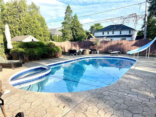 view of swimming pool with a patio, a pool with connected hot tub, a water slide, a fenced backyard, and a diving board