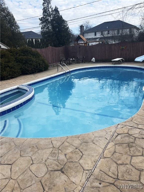 view of pool featuring a diving board, a patio, fence, and a pool with connected hot tub