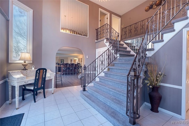 foyer with stairs, arched walkways, baseboards, and tile patterned floors