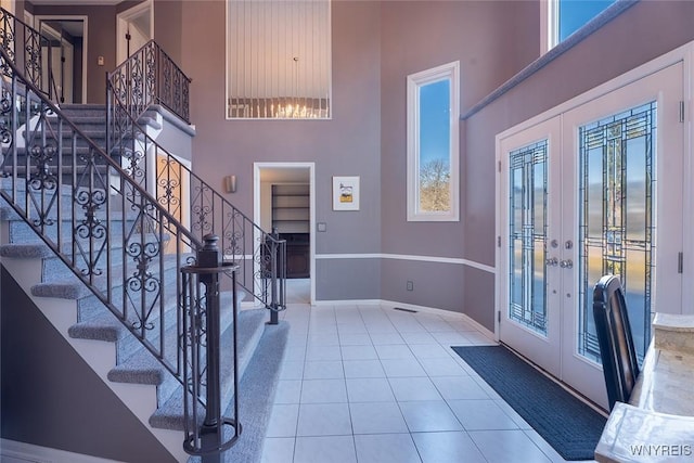 tiled entrance foyer with french doors, stairway, a towering ceiling, and baseboards