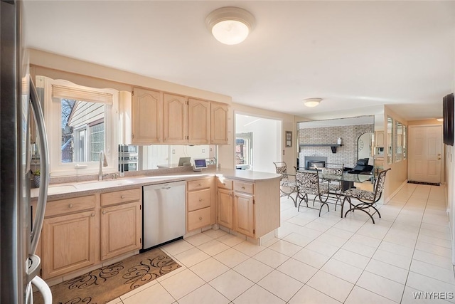 kitchen featuring stainless steel appliances, light countertops, light brown cabinetry, open floor plan, and a sink