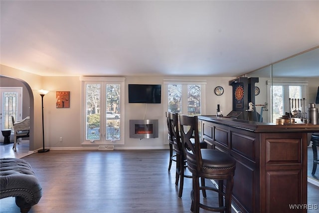 bar with arched walkways, dark wood-style flooring, a glass covered fireplace, and visible vents