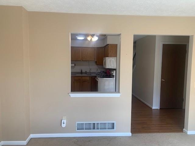 kitchen featuring carpet floors, visible vents, white microwave, range with electric cooktop, and baseboards