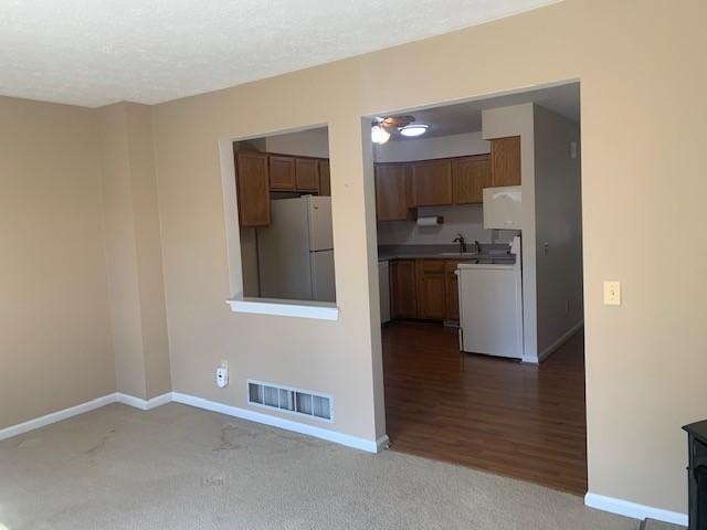 kitchen with visible vents, freestanding refrigerator, carpet flooring, a sink, and baseboards