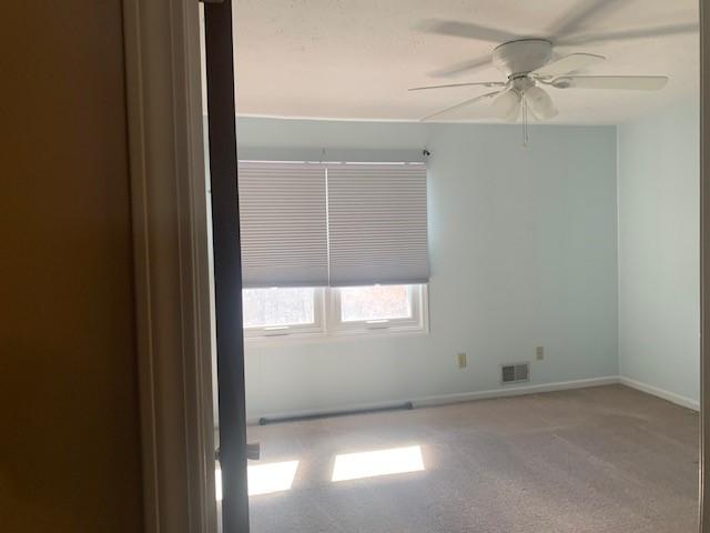 carpeted spare room with a ceiling fan, visible vents, and baseboards