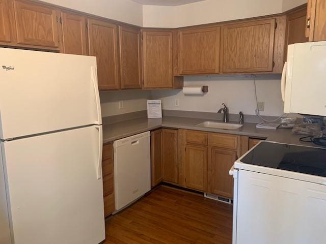 kitchen featuring dark wood-type flooring, white appliances, brown cabinetry, and a sink