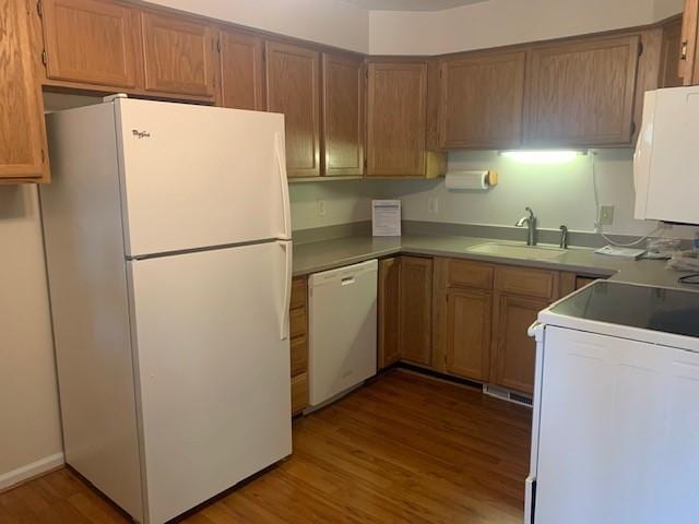 kitchen with wood finished floors, white appliances, a sink, and brown cabinets