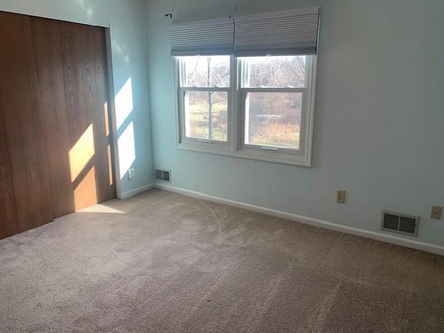 spare room with light carpet, visible vents, and baseboards