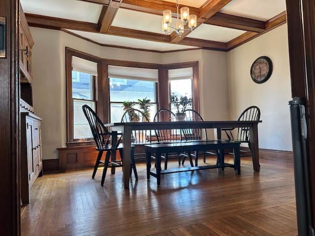 dining area featuring beamed ceiling, coffered ceiling, dark wood finished floors, an inviting chandelier, and crown molding