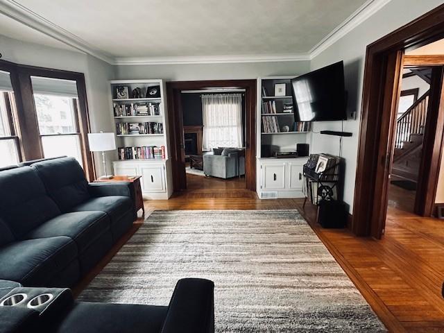 living area with plenty of natural light, wood finished floors, and ornamental molding