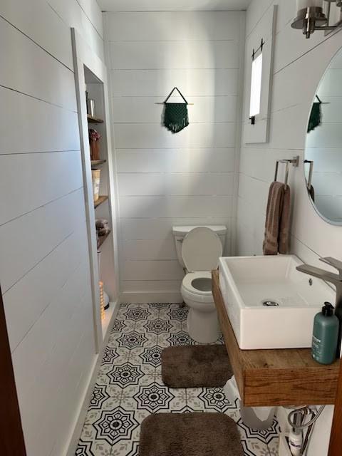 bathroom featuring a sink, walk in shower, tile patterned floors, toilet, and tile walls