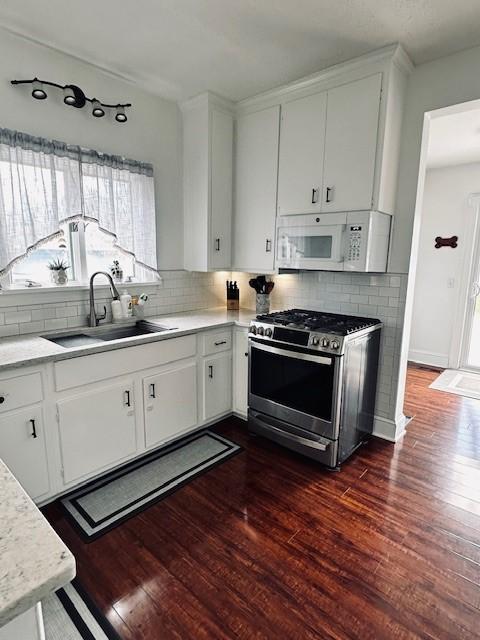 kitchen featuring dark wood-type flooring, a sink, backsplash, white microwave, and stainless steel gas range