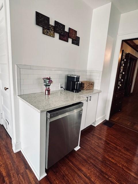 kitchen featuring stainless steel dishwasher, backsplash, dark wood-style floors, and white cabinetry