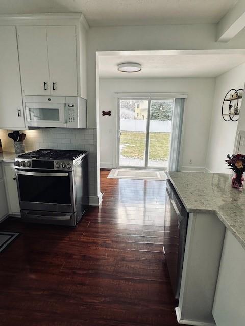 kitchen featuring light stone countertops, decorative backsplash, appliances with stainless steel finishes, white cabinets, and dark wood-style flooring