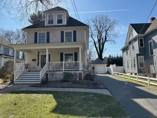 american foursquare style home featuring a detached garage, fence, a front yard, covered porch, and an outbuilding