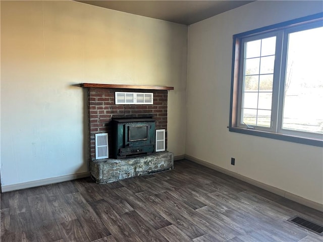 unfurnished living room featuring a wood stove, dark wood finished floors, visible vents, and baseboards