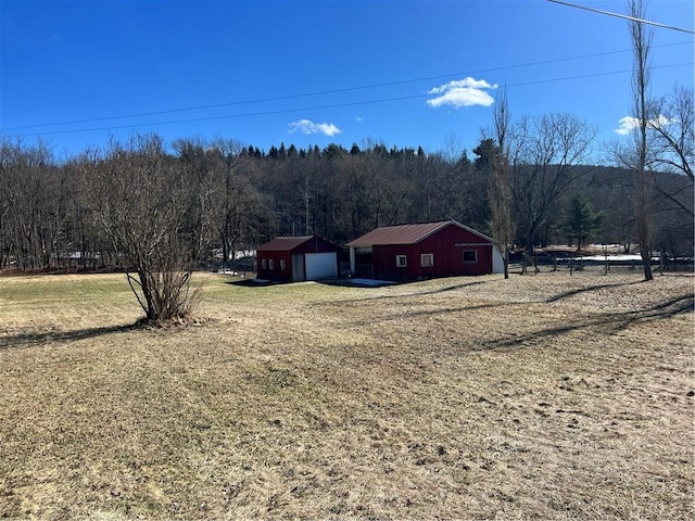 view of yard featuring driveway, an outbuilding, a view of trees, and an outdoor structure