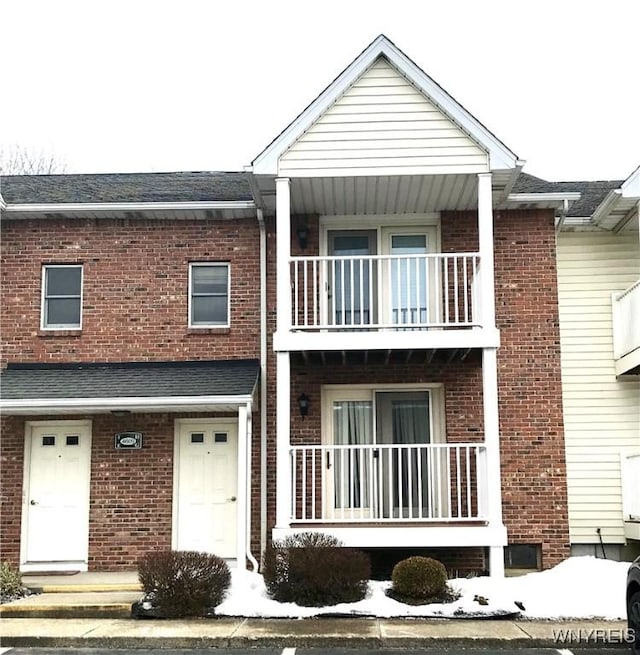 view of property featuring brick siding, a porch, and a balcony