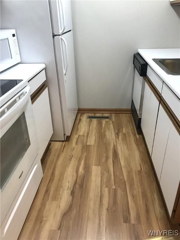 kitchen featuring visible vents, light wood-style flooring, white appliances, white cabinets, and light countertops