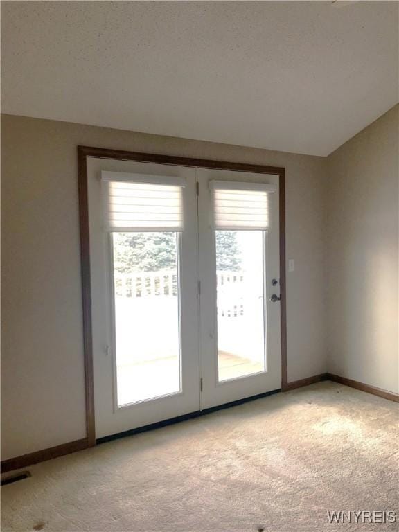 doorway with a textured ceiling, baseboards, and light carpet