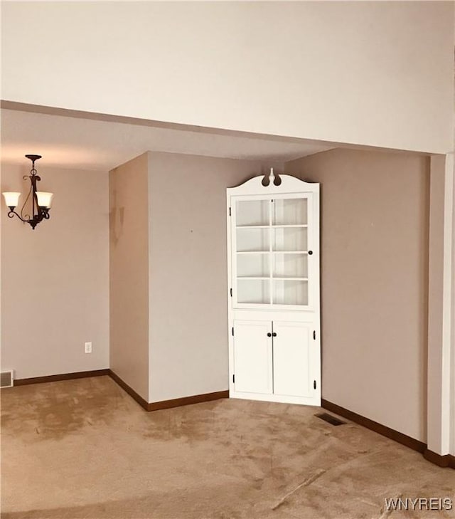 spare room featuring a notable chandelier, light colored carpet, visible vents, and baseboards